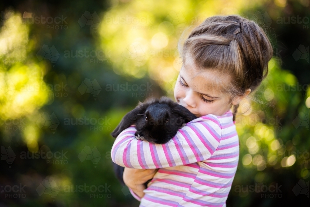 Happy little girl cuddling black pet bunny rabbit - Australian Stock Image