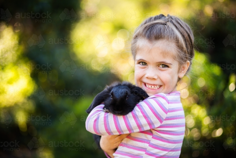 Happy little girl cuddling black pet bunny rabbit - Australian Stock Image