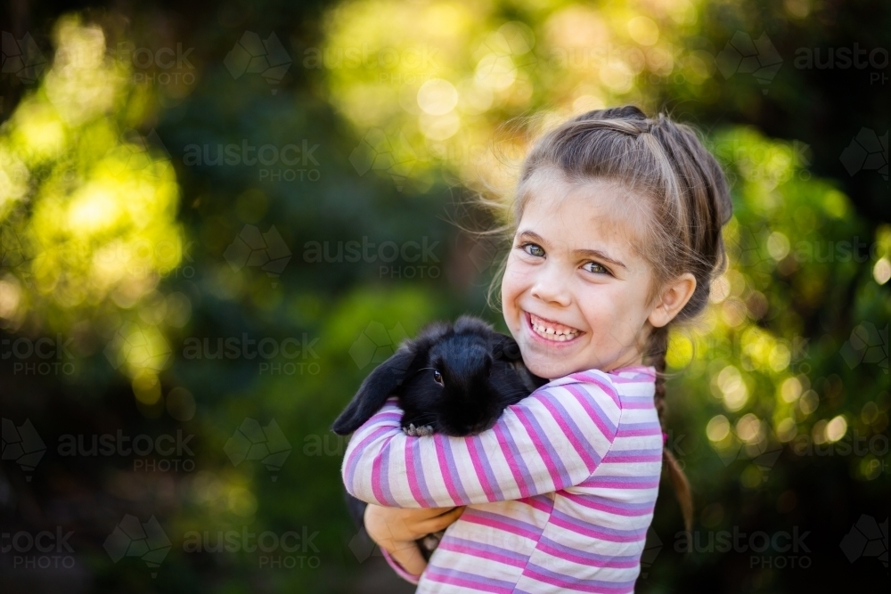 Happy little girl cuddling black pet bunny rabbit - Australian Stock Image