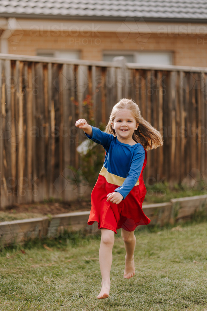 Happy little girl in a superhero costume running around backyard - Australian Stock Image