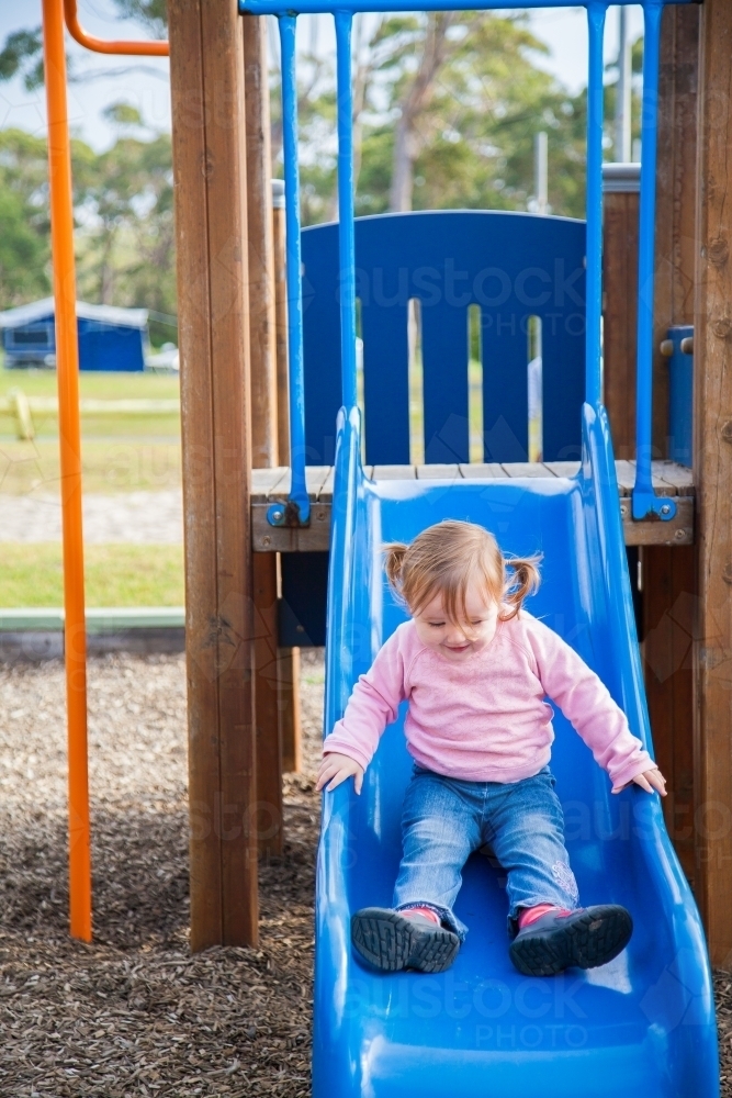 Image of Happy little girl in pink going down a slide Austockphoto