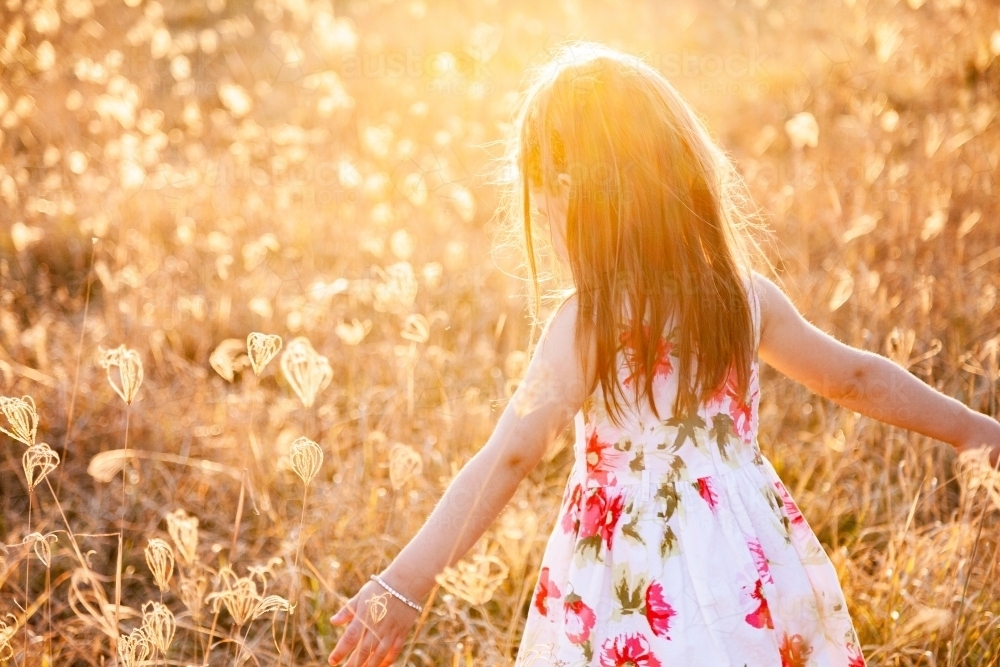 Happy little girl laughing and spinning in sunlit grass - Australian Stock Image