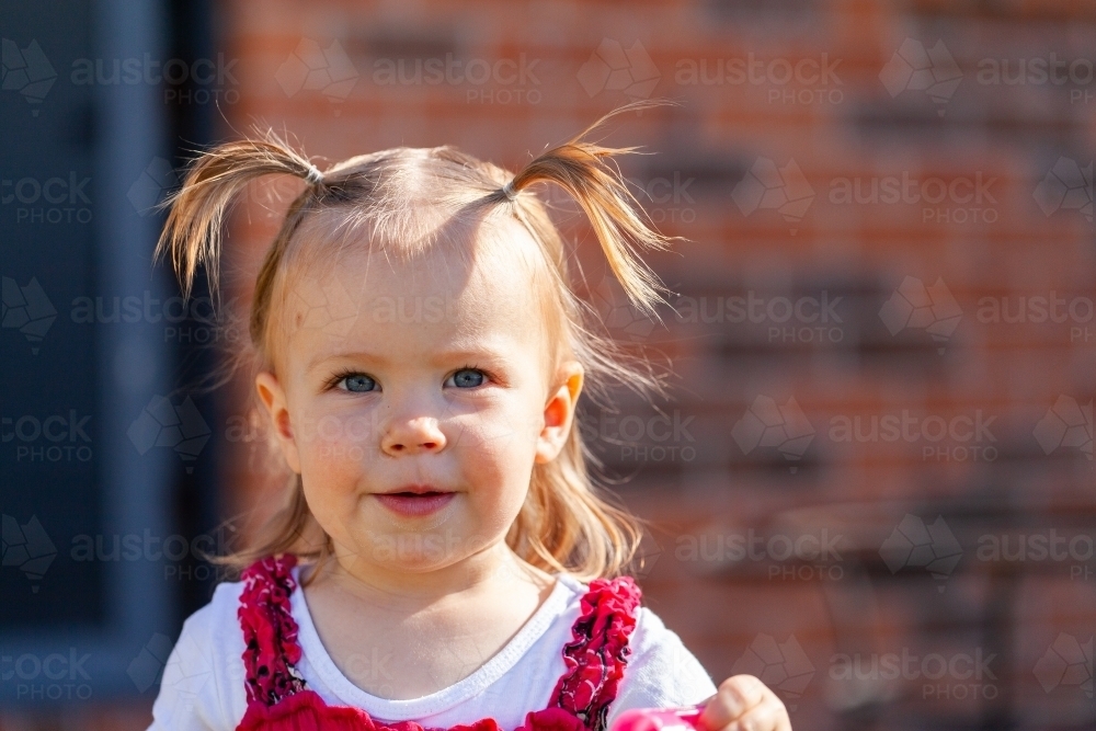 Happy little girl outside home with hair in pigtails - Australian Stock Image