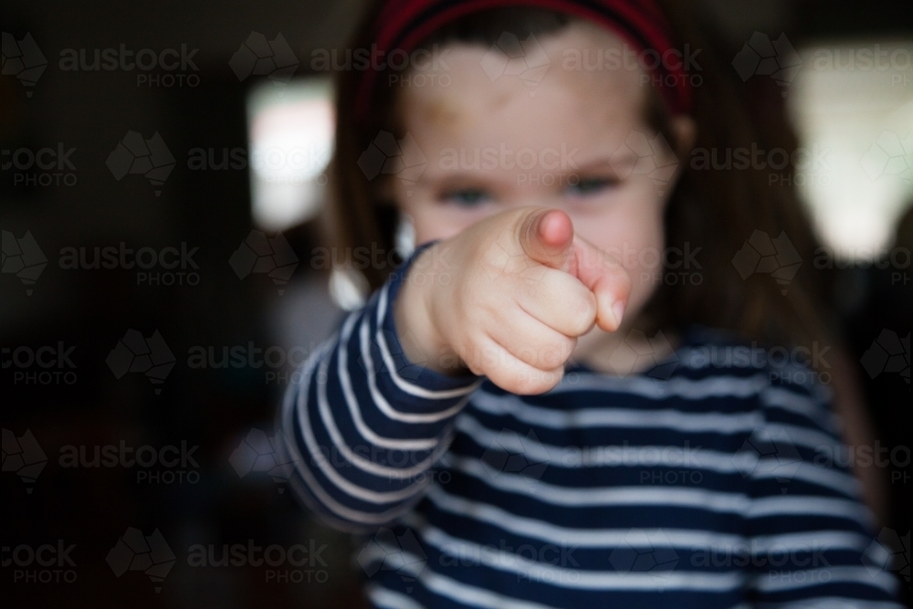 Happy little girl pointing at camera focus on finger - Australian Stock Image