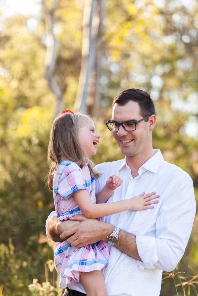 Happy little girl with cerebral palsy laughing as her dad holds her outside - Australian Stock Image