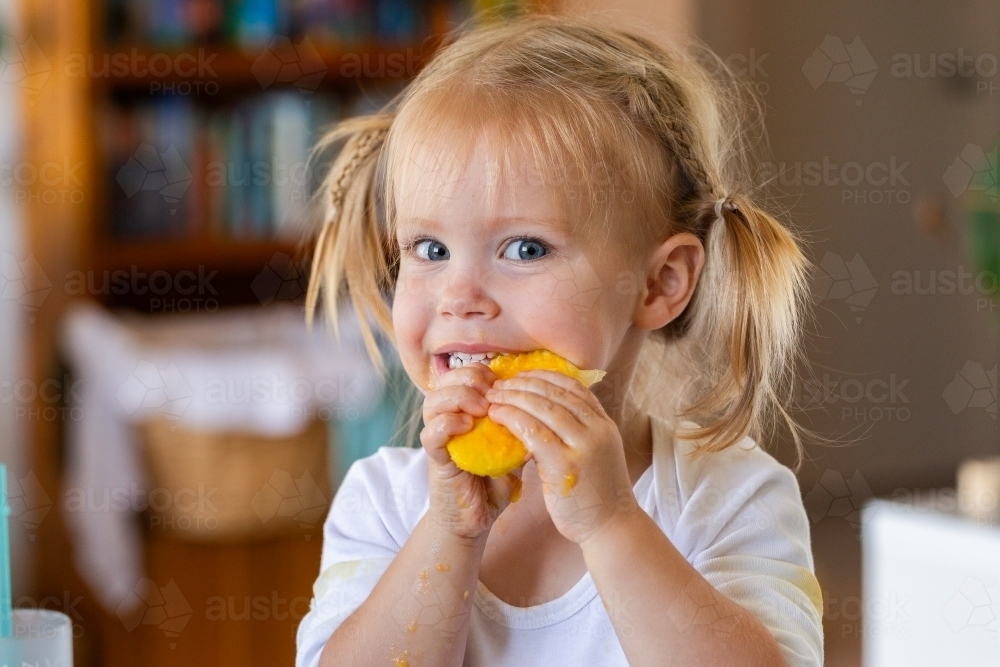 Happy little kid eating mango seed and getting sticky - Australian Stock Image