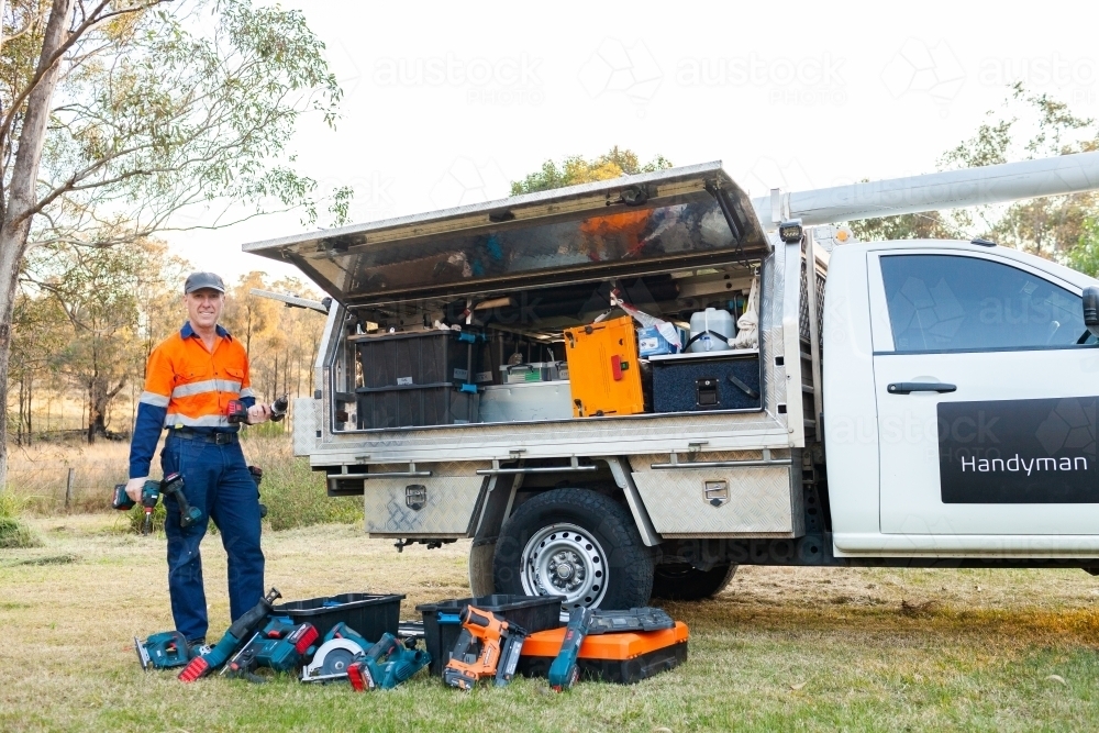 Happy middle aged handyman with work ute showing off power tools - Australian Stock Image