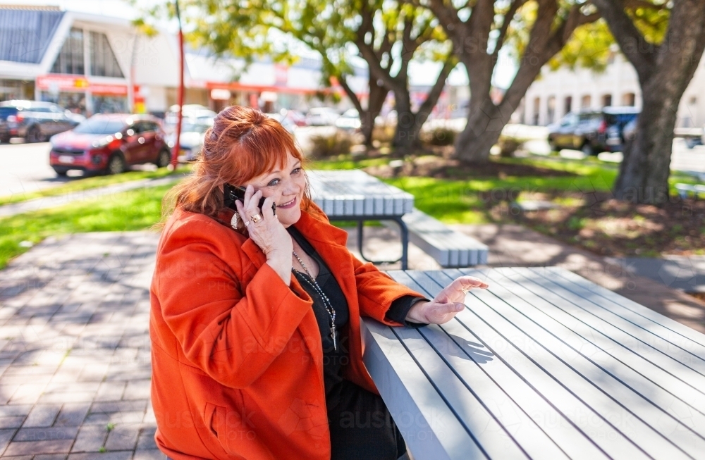 Happy middle aged woman on phone call in small park in town - Australian Stock Image