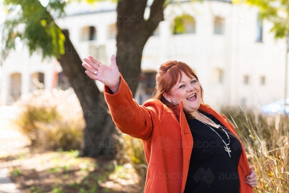 Happy middle aged woman waving hi hello outside in park - Australian Stock Image