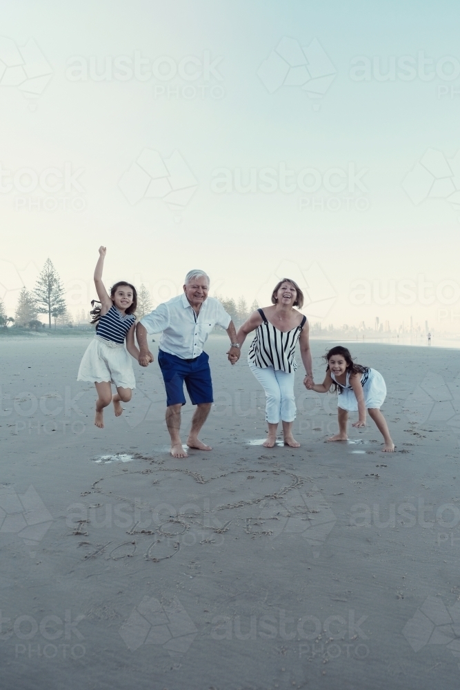 Happy multicultural grandparent with grandchildren on the beach - Australian Stock Image