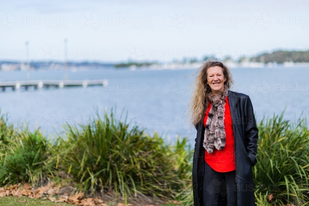 Happy older aussie woman with indigenous heritage standing beside water at Speers Point - Australian Stock Image