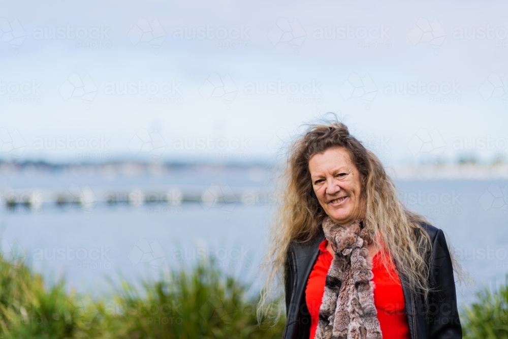 Happy older aussie woman with indigenous heritage standing beside water at Speers Point - Australian Stock Image