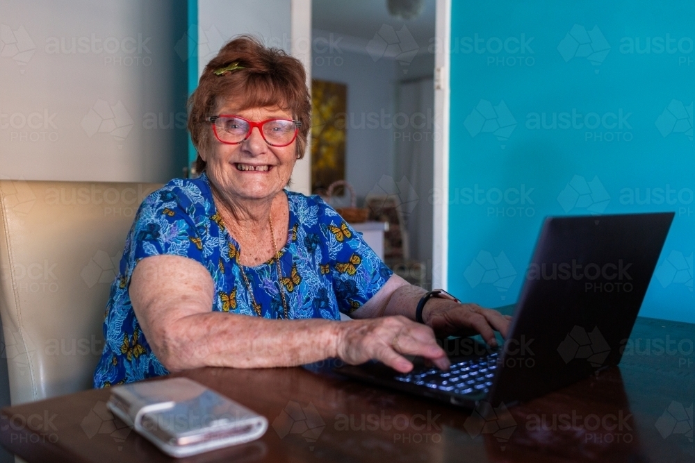 Happy older woman working on laptop at table - Australian Stock Image