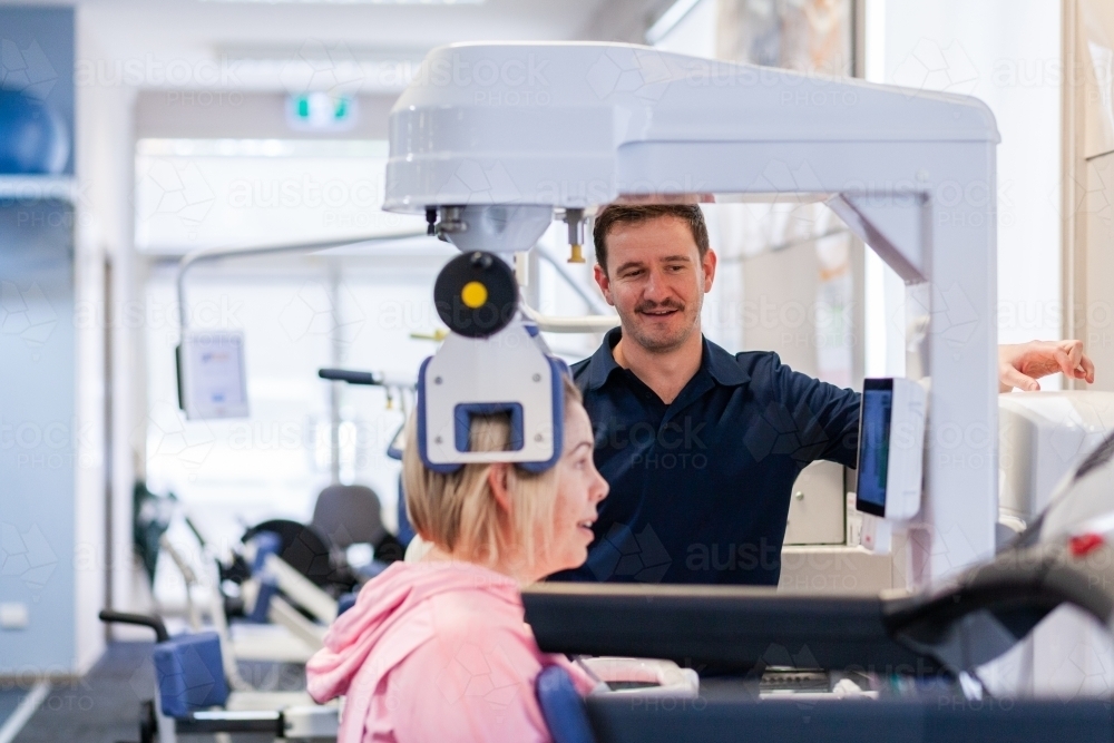 Happy physio standing beside woman using physical therapy equipment - Australian Stock Image