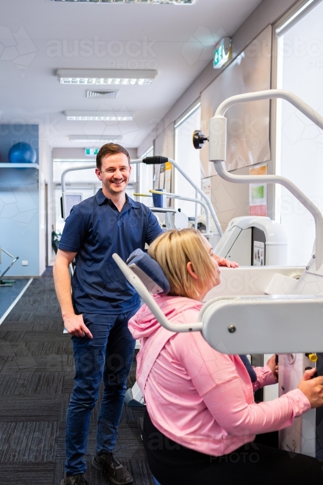 Happy physio standing with female client using medical exercise equipment to promote healing - Australian Stock Image