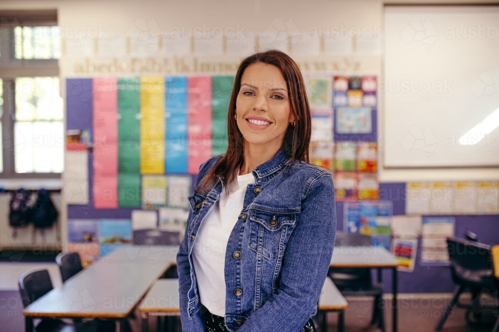 Happy primary school teacher in classroom smiling at camera - Australian Stock Image