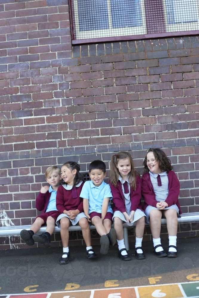 Happy school children sitting outside their school building - Australian Stock Image