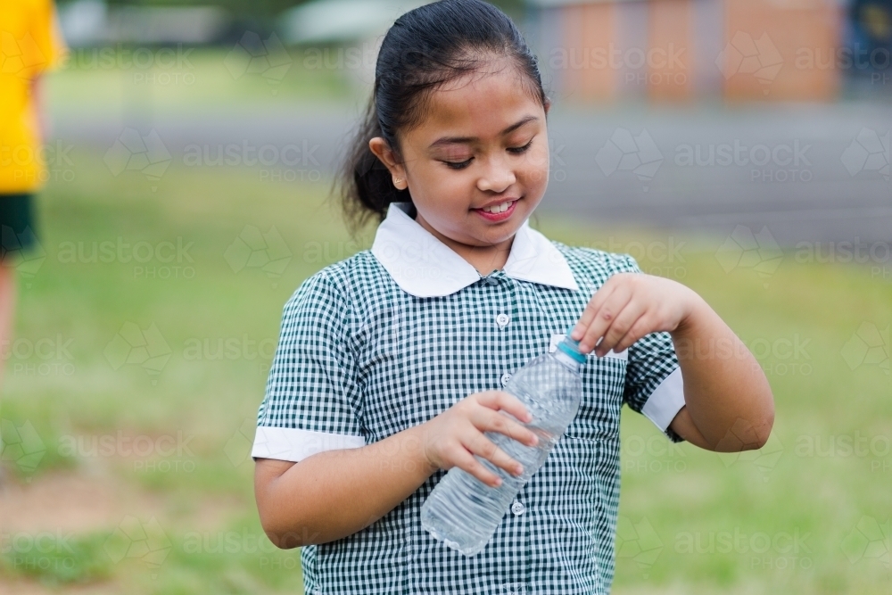 Happy school girl holding plastic water bottle - Australian Stock Image