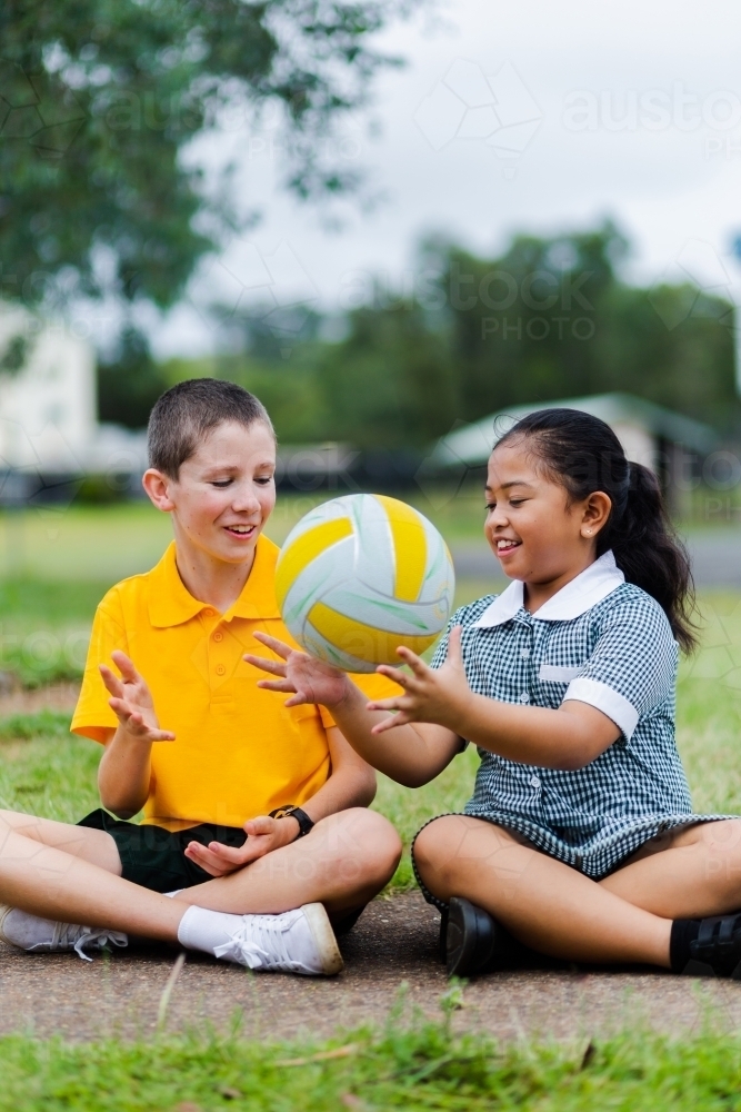 Happy school students passing a ball laughing and smiling together - Australian Stock Image