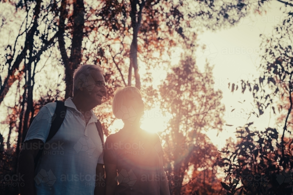 Happy senior couple on a nature walk, with sun flare - Australian Stock Image