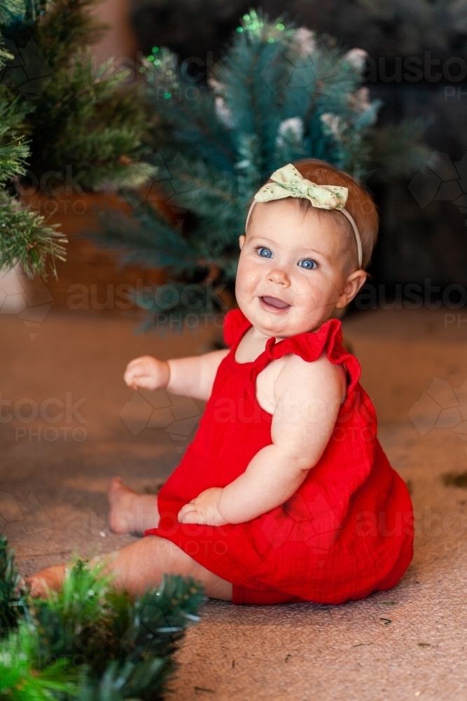 happy seven month old baby sitting on floor near Christmas tree - Australian Stock Image