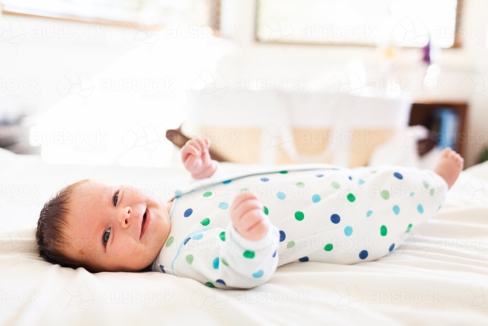 Happy smiling baby lying on parents bed in morning one month old - Australian Stock Image