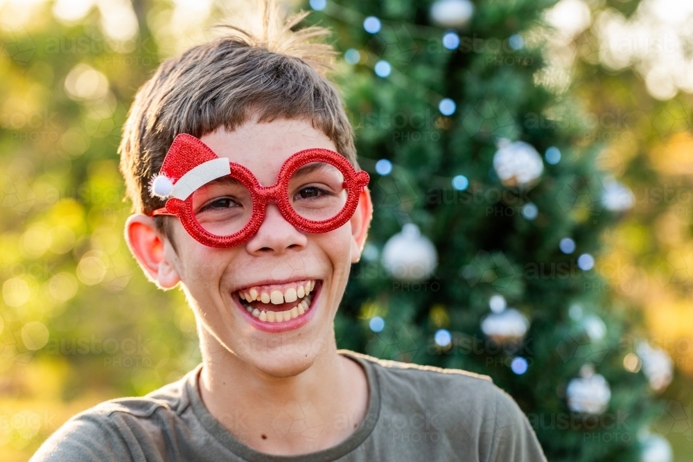 Happy smiling boy wearing silly Christmas glasses outside - Australian Stock Image