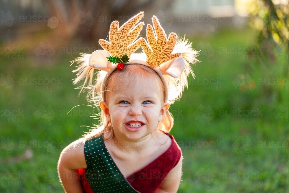 Happy smiling little girl in Christmas colours and wearing deer antler headband - Australian Stock Image