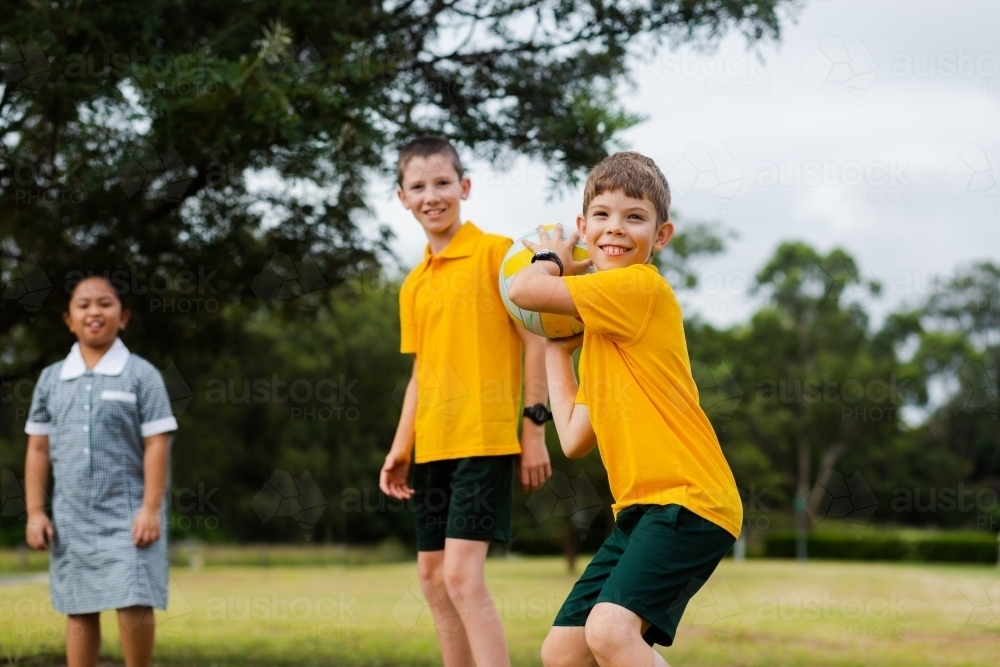 Happy smiling school boy throwing ball outside - Australian Stock Image