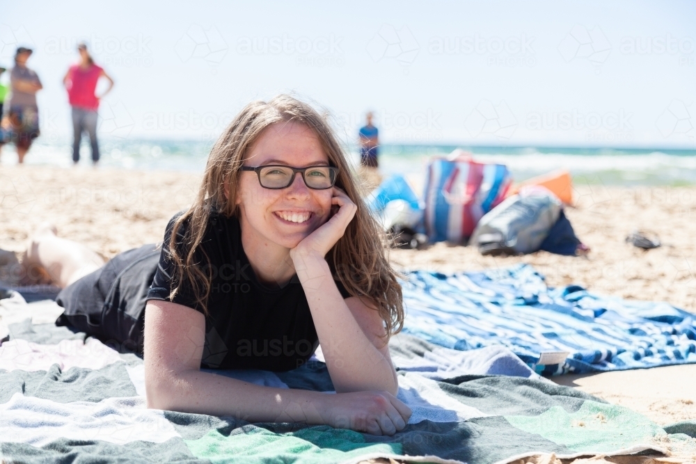 Happy teen girl lying on beach towel at the seaside - Australian Stock Image