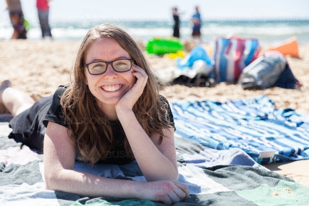 Happy teen girl lying on beach towel at the seaside - Australian Stock Image