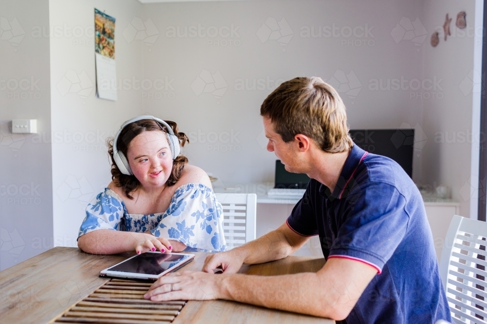 Happy teen wearing headphones talking at table with OT NDIS worker - Australian Stock Image