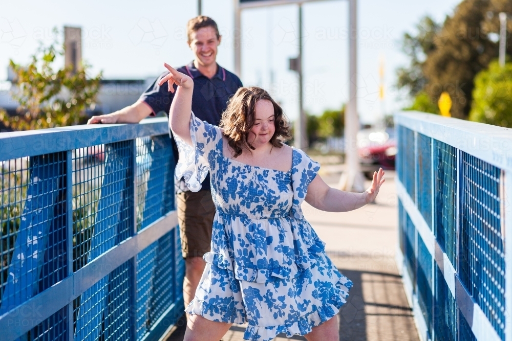 Happy teenage girl with down syndrome dancing on blue footbridge - Australian Stock Image