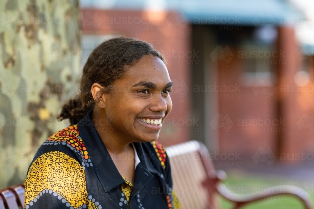 happy teenaged aboriginal girl sitting on bench in shade - Australian Stock Image