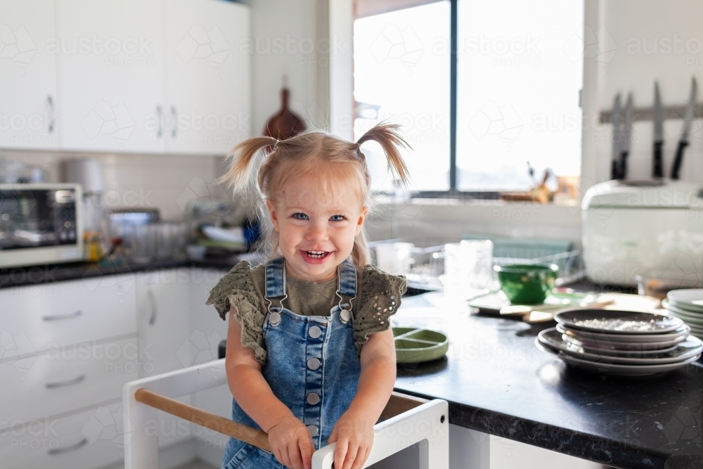 Image of Happy toddler girl standing in messy kitchen with dishes piled ...