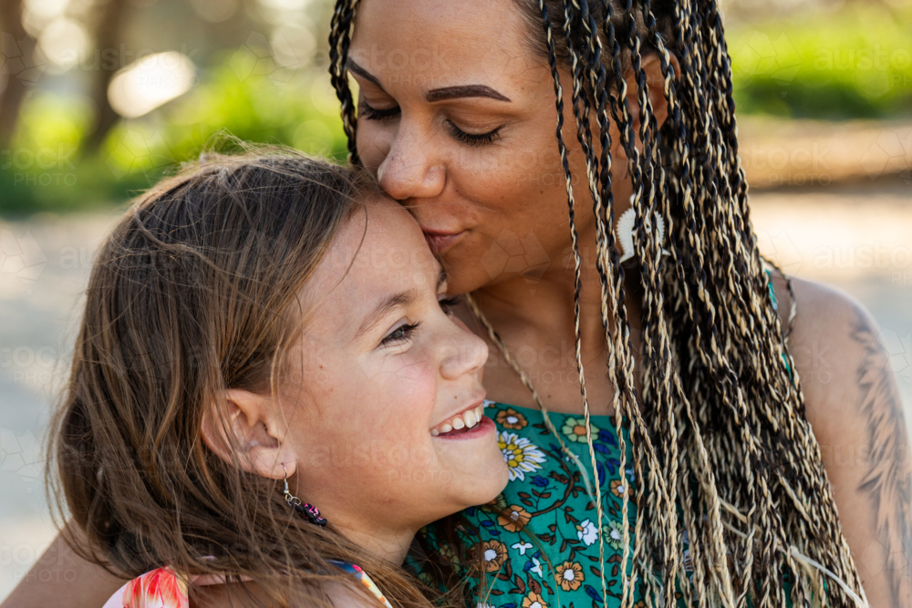 Happy Torres Strait Islander woman holding her nine year old daughter and kissing her forehead - Australian Stock Image