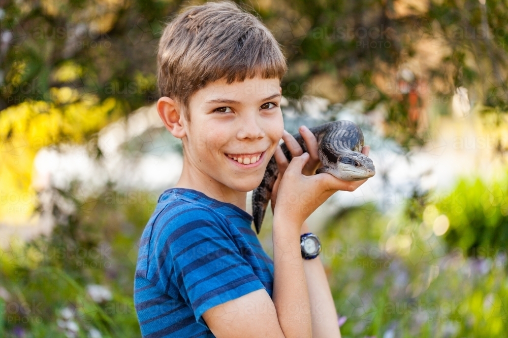 Happy tween boy with blue-tongued lizard outside in garden - Australian Stock Image