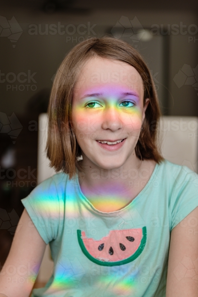 Happy tween girl with rainbow shadow on her face - Australian Stock Image