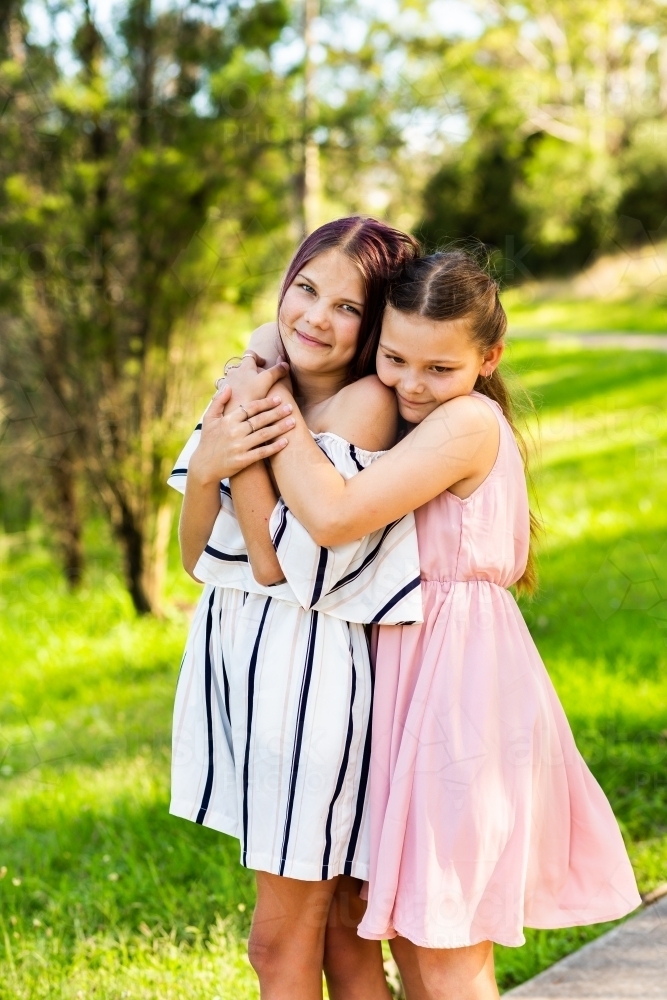 Happy tween sisters hug outside in park - Australian Stock Image