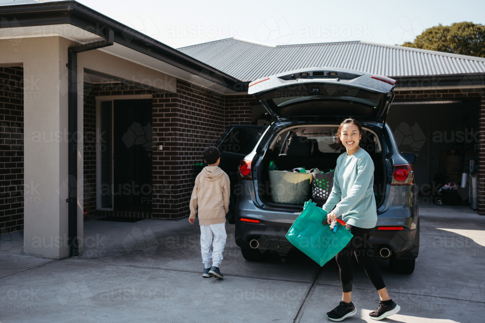 happy woman carrying a reusable shopping bag from the car boot - Australian Stock Image