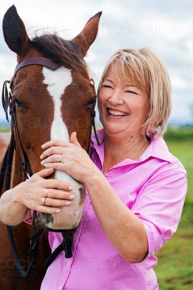 Happy woman standing at her horses head holding bridle - Australian Stock Image