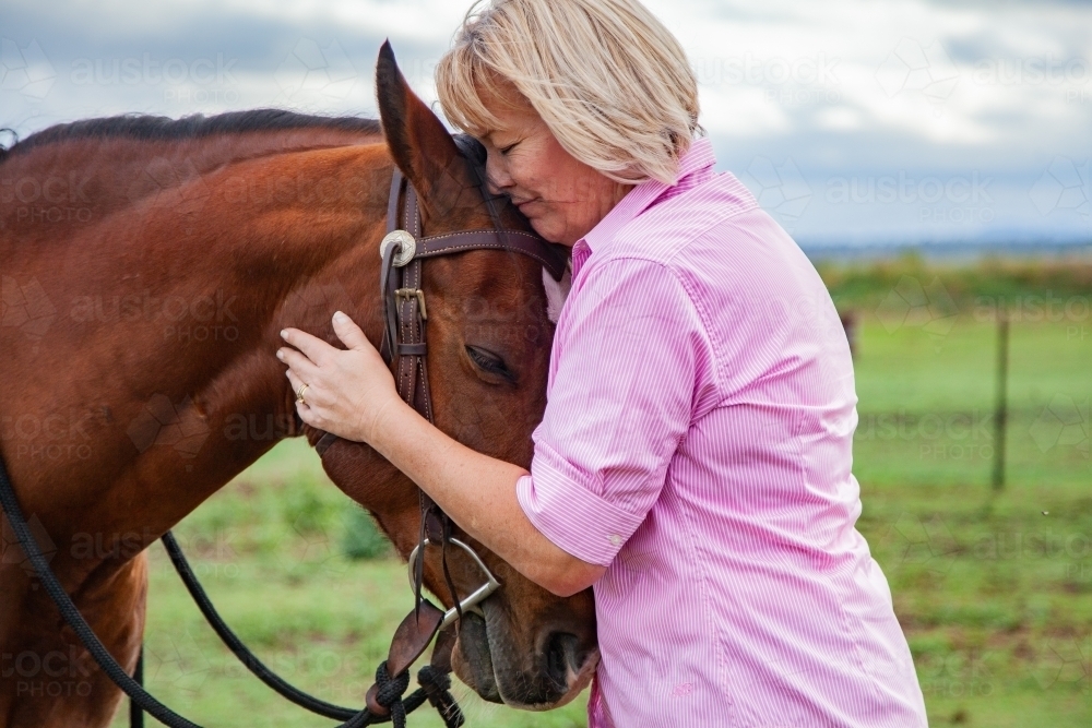 Happy woman standing at her horses head holding bridle - Australian Stock Image