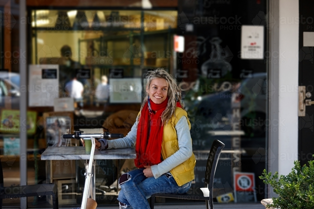 Happy woman with dreadlocks at cafe with electric scooter - Australian Stock Image