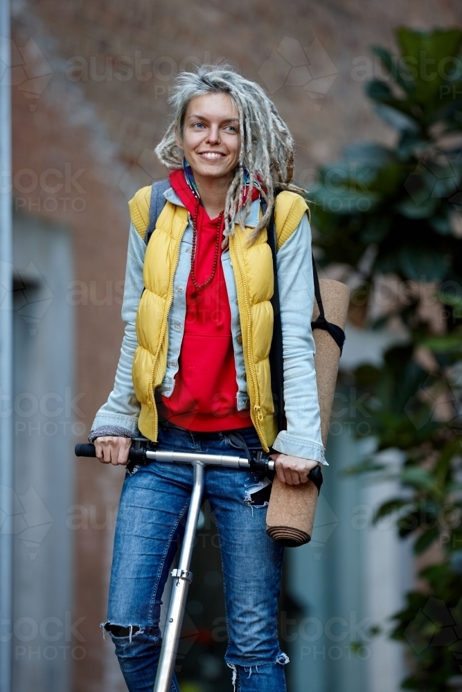 Happy Woman with dreadlocks on electric scooter going to yoga class - Australian Stock Image