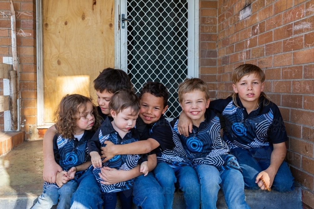 Happy young Aboriginal kids sitting together on doorstep of home - Australian Stock Image