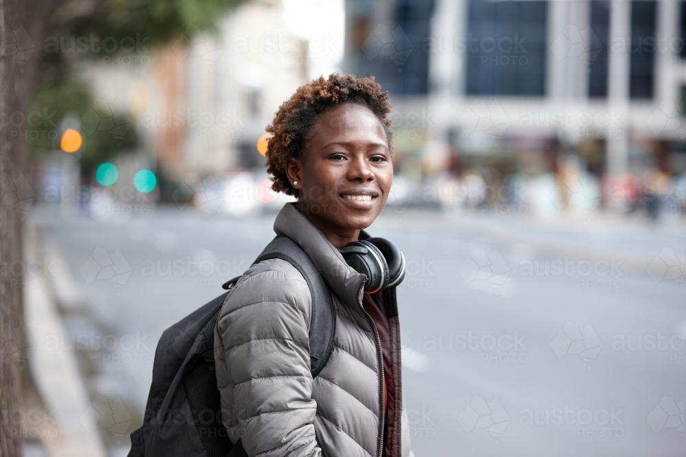 Happy young African woman wearing wireless headphones in city - Australian Stock Image