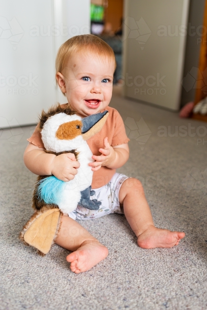 Happy young aussie baby holding plush toy kookaburra - Australian Stock Image