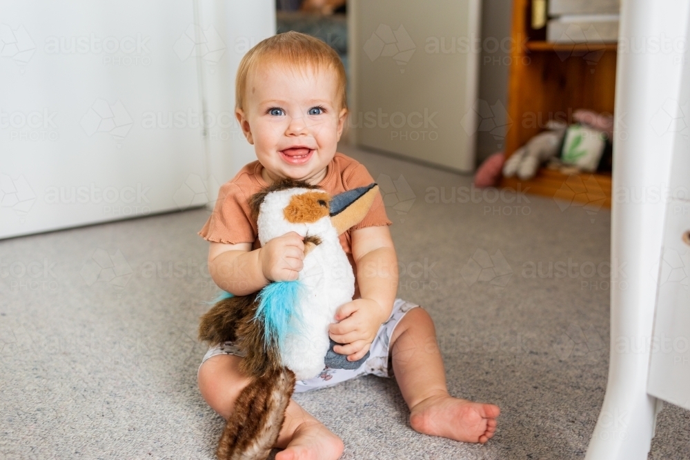 Happy young aussie baby holding plush toy kookaburra - Australian Stock Image