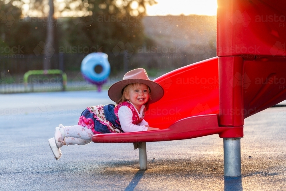 Happy young Australian girl sliding down slippery dip slide at park - Australian Stock Image