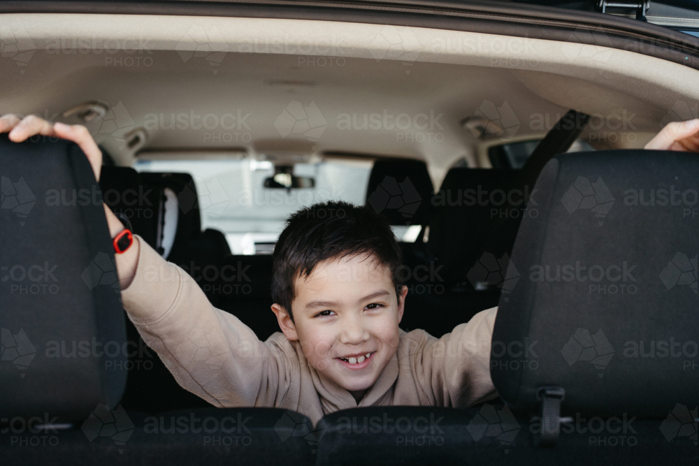 Happy young boy in the backseat looking out the boot of car ready for trip - Australian Stock Image